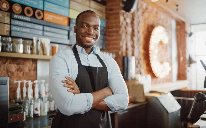 Man die met zijn armen gekruist staat achter de bar