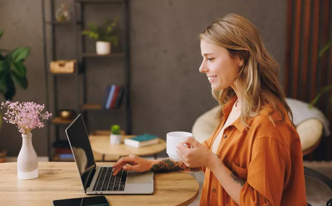 Une femme souriante lit quelque chose sur son ordinateur portable.