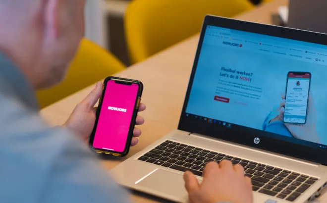 Un homme consultant l'application NOWJOBS via un smartphone et un ordinateur portable